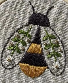 a close up of a embroidery on a piece of cloth with flowers and a bug