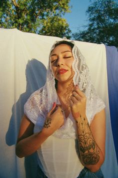 a woman with tattoos on her arms and chest standing in front of a white sheet