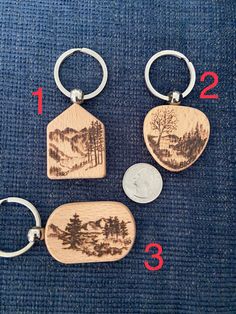 four wooden keychains with trees and mountains on them are shown in three different sizes