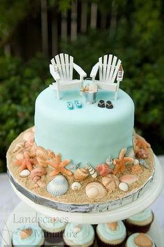 there is a blue cake with two chairs on it and seashells in the sand