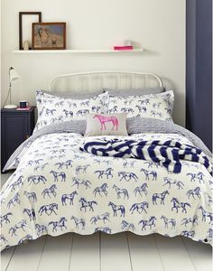 a white bed with blue and pink horses on the comforter, pillows and pillow cases