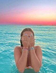 a girl covers her face while floating in the ocean at sunset or sunrise with both hands