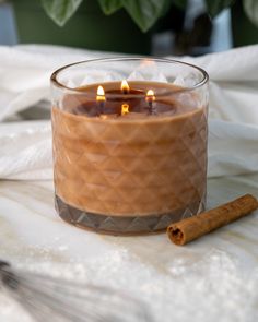 a glass candle sitting on top of a table next to a cinnamon stick and potted plant