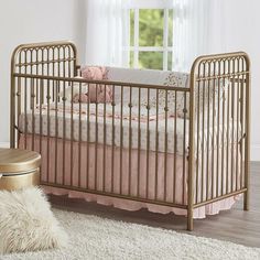 a baby crib with pink and white bedding next to a window