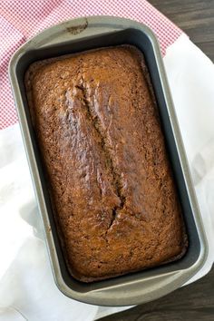 a loaf of banana bread sitting in a pan on top of a table next to a red and white checkered napkin