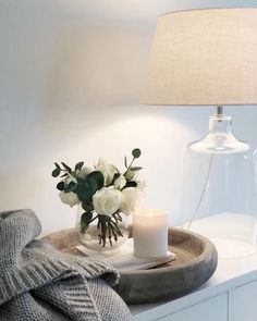 a vase with white flowers and a lit candle on a table next to a blanket