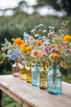 colorful vases filled with wildflowers sit on a wooden table in front of trees