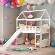 there is a white bunk bed with a slide in front of it and balloons all around the room