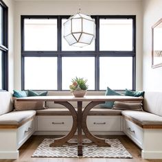 a table with some pillows on it in front of two windows and a window seat