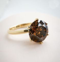 a fancy ring with a large brown diamond on the front and side, sitting on a white surface