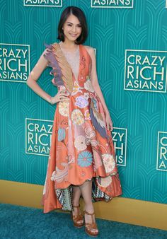 a woman standing on top of a blue carpet wearing a dress with flowers and leaves