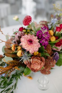 an arrangement of flowers on a white table cloth with wine glasses in the foreground