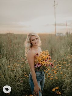 a woman standing in the middle of a field with flowers on her chest and holding a bouquet