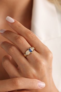 a woman's hand wearing a gold ring with blue and white stones on it