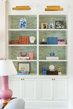 a white bookcase filled with lots of books on top of a wooden table next to a lamp