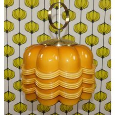 a yellow lamp hanging from the ceiling in front of a wallpapered background with green leaves