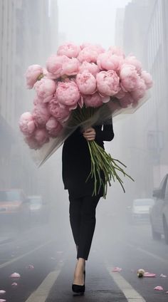 a woman is walking down the street with pink flowers on her head and holding a large bouquet of peonies