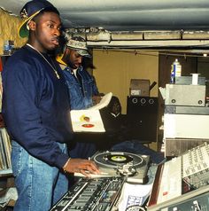 two men standing next to each other in front of a mixing desk with records on it