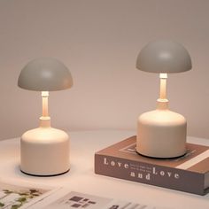 two white lamps sitting on top of a table next to a book and an open magazine