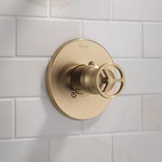 a bathroom faucet mounted on a white tiled wall with gold trim and knobs