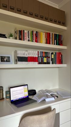 a laptop computer sitting on top of a desk next to a shelf filled with books