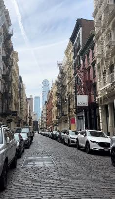 cars parked on the side of a brick road in an urban area with tall buildings