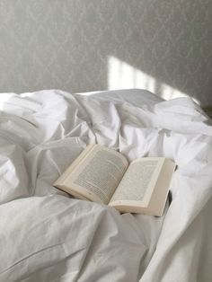 an open book laying on top of a white bed