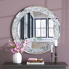 a round mirror sitting on top of a dresser next to a vase filled with flowers