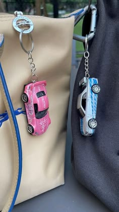 two purses with cars attached to them, one is pink and the other is blue