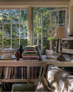 there is a table with books on it and a lamp in front of the window