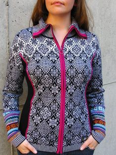 a woman standing in front of a wall wearing a black and white jacket with pink trim