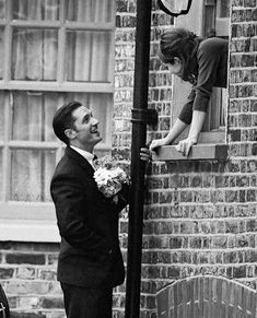 a man in a suit and tie standing next to a woman on a window sill