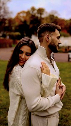 a man and woman standing next to each other in the grass with their arms around each other