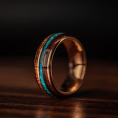 a wedding ring with blue and green inlays on it, sitting on a wooden surface