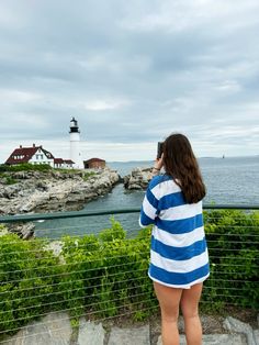 a woman standing on steps looking at the ocean with a light house in the background