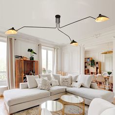 a living room filled with white furniture and lots of lights above the couches in front of large windows