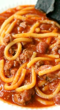 a white plate topped with spaghetti and meat in tomato sauce next to a black napkin