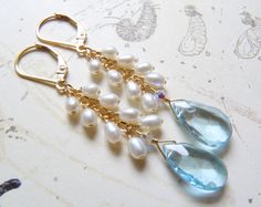 Stunning statement earrings feature gorgeous sought after genuine teardrop shaped blue topaz gemstones. White freshwater pearls cascade on a 14k gold filled chain. Set on 14k gold filled leverback earring closures. Artisan blue topaz earrings makes for a thoughtful gift for a woman born in December since blue topaz is her birthstone. Earring Details: - Earring length is 2.25 inches long with the earring closure shown - The blue topaz gemstone is .75 inches long and .4 inches wide - 14k gold fill