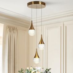 three lights hanging from a ceiling in a room with white walls and flowers on the table