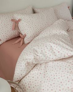 a bed with pink and white sheets and pillows on top of it next to a night stand