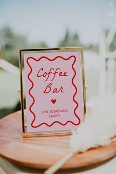 a coffee bar sign sitting on top of a wooden table next to a white feather