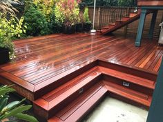 a wooden deck with steps leading up to the top and bottom level, surrounded by greenery