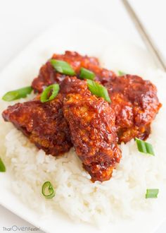 two pieces of meat covered in sauce on top of rice with green onions and scallions