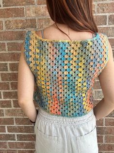 a woman standing in front of a brick wall wearing a multicolored crochet top