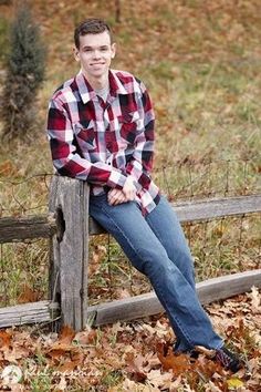 a young man sitting on top of a wooden fence