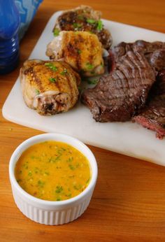 a small white bowl filled with soup on top of a wooden table next to a sandwich