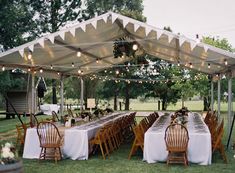 an outdoor tent with tables and chairs set up for dinner under string lights, surrounded by greenery