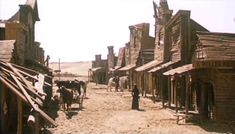 an old western town with wooden buildings and people walking down the street in front of them