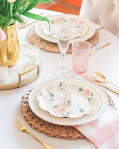 the table is set with plates, silverware and pink flowers