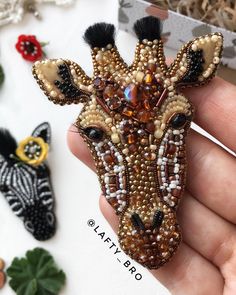 a hand holding a beaded giraffe brooch